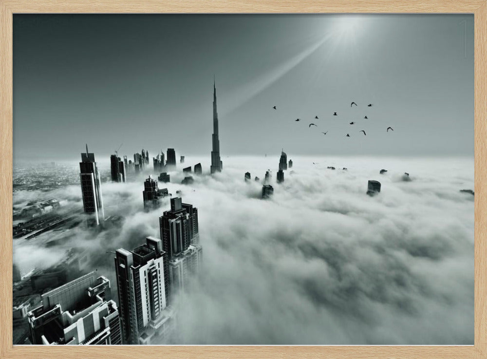 A framed, black and white aerial photograph of the Dubai skyline piercing through a thick layer of clouds. The Burj Khalifa stands prominently in the center, with other skyscrapers emerging from the fog. A flock of birds flies in the sky as a bright sunbeam shines down from the upper right corner. Wall Art