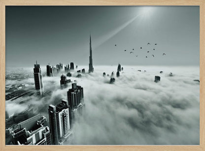 A framed, black and white aerial photograph of the Dubai skyline piercing through a thick layer of clouds. The Burj Khalifa stands prominently in the center, with other skyscrapers emerging from the fog. A flock of birds flies in the sky as a bright sunbeam shines down from the upper right corner. Wall Art