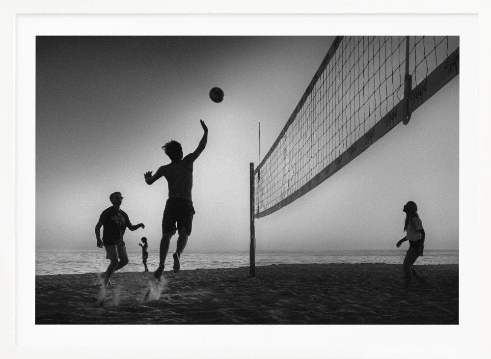 A black and white action shot of people playing volleyball on a beach, presented in a silver frame. The scene is silhouetted against a light sky, likely during sunrise or sunset. One player is captured mid-jump, arm raised to hit the ball over the net. Other players are visible on the sand, with the ocean in the background. Decor