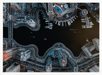 A dramatic top-down aerial photograph of a sprawling modern city at night. A dark waterway curves through the center, surrounded by illuminated skyscrapers, busy roads, and a marina packed with boats, all within a silver picture frame. Artwork