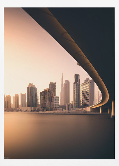 A view of the Dubai skyline, including the Burj Khalifa, framed by the sweeping curve of a bridge in the foreground. The city is bathed in the warm, soft light of a sunrise or sunset, with its reflection visible on the calm water below. Decor