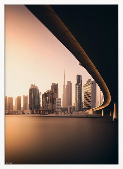 A view of the Dubai skyline, including the Burj Khalifa, framed by the sweeping curve of a bridge in the foreground. The city is bathed in the warm, soft light of a sunrise or sunset, with its reflection visible on the calm water below. Decor