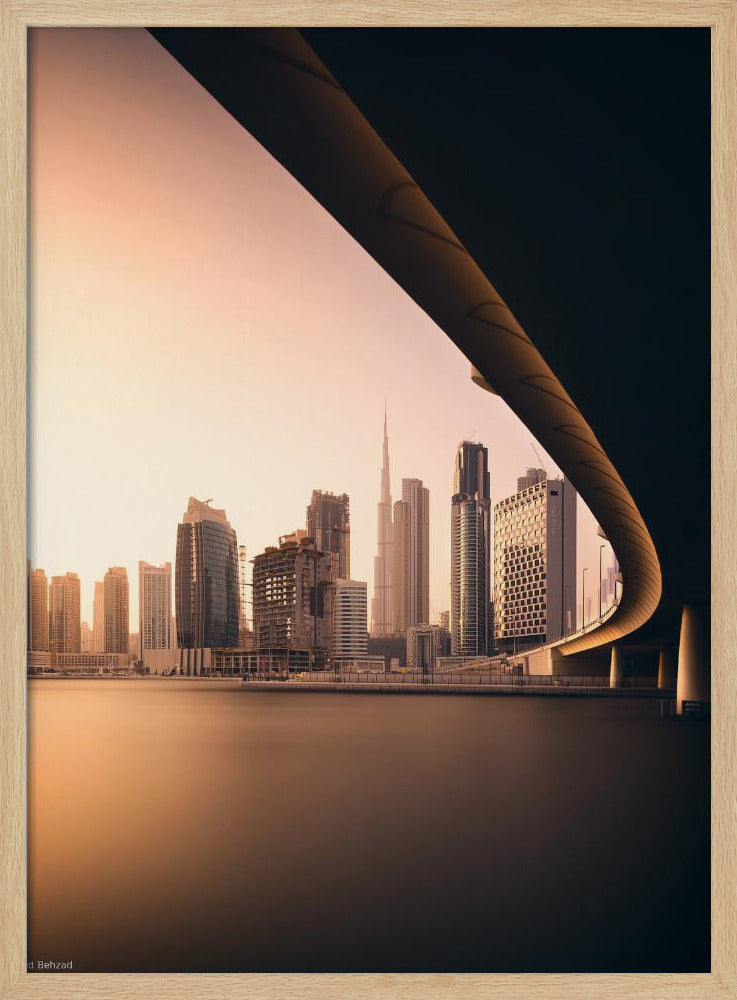 A view of the Dubai skyline, including the Burj Khalifa, framed by the sweeping curve of a bridge in the foreground. The city is bathed in the warm, soft light of a sunrise or sunset, with its reflection visible on the calm water below. Decor