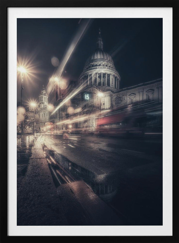 A dynamic long-exposure photograph of a wet London street at night, with the iconic dome of St. Paul's Cathedral illuminated in the background. Streaks of light from passing traffic, including a red bus, blur across the scene, while the glistening pavement reflects the cathedral and bright streetlights. Decor