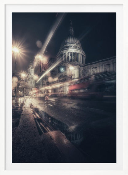 A dynamic long-exposure photograph of a wet London street at night, with the iconic dome of St. Paul's Cathedral illuminated in the background. Streaks of light from passing traffic, including a red bus, blur across the scene, while the glistening pavement reflects the cathedral and bright streetlights. Decor