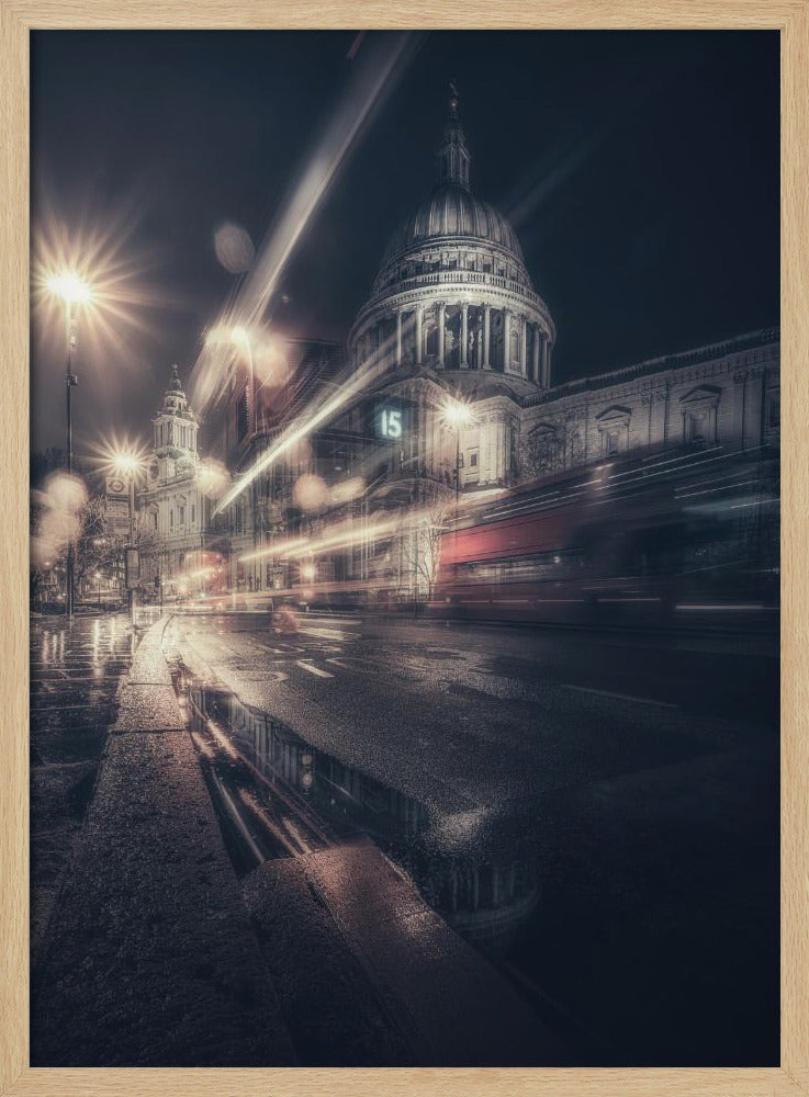 A dynamic long-exposure photograph of a wet London street at night, with the iconic dome of St. Paul's Cathedral illuminated in the background. Streaks of light from passing traffic, including a red bus, blur across the scene, while the glistening pavement reflects the cathedral and bright streetlights. Decor