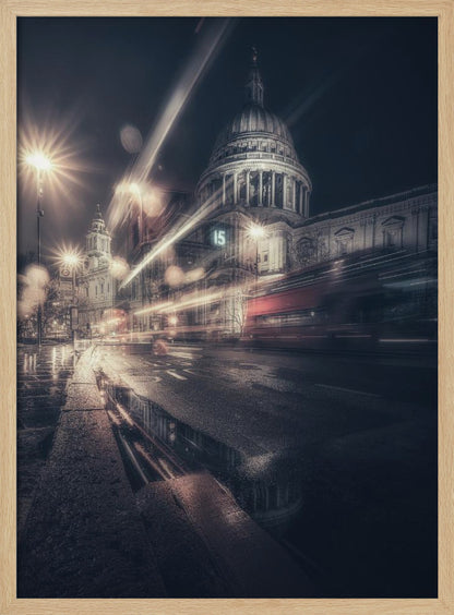 A dynamic long-exposure photograph of a wet London street at night, with the iconic dome of St. Paul's Cathedral illuminated in the background. Streaks of light from passing traffic, including a red bus, blur across the scene, while the glistening pavement reflects the cathedral and bright streetlights. Decor