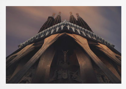 A dramatic, low-angle shot of the Sagrada Familia cathedral, focusing on the intricate details of the Passion Facade against a dusky purple and orange sky. The spires tower above, while deep shadows highlight the unique, angled columns and the central sculpture of the crucifixion. Poster