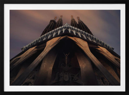 A dramatic, low-angle shot of the Sagrada Familia cathedral, focusing on the intricate details of the Passion Facade against a dusky purple and orange sky. The spires tower above, while deep shadows highlight the unique, angled columns and the central sculpture of the crucifixion. Poster