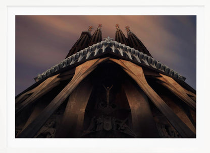 A dramatic, low-angle shot of the Sagrada Familia cathedral, focusing on the intricate details of the Passion Facade against a dusky purple and orange sky. The spires tower above, while deep shadows highlight the unique, angled columns and the central sculpture of the crucifixion. Poster