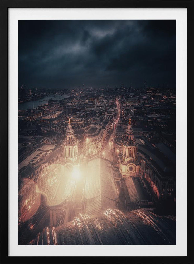 A dramatic, high-angle nighttime photograph of a sprawling city, likely London, viewed from the top of a cathedral. The foreground shows the curved dome, while below, two towers and the long roof of the church are brightly illuminated. The city stretches into the distance with countless golden lights under a dark, stormy, and cloud-filled sky. Poster
