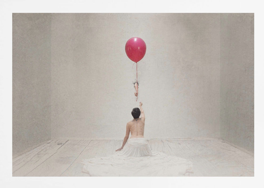 A surreal fine art photograph of a person with a bare back and a long white skirt, sitting on the floor of a minimalist grey room. They are reaching up towards a small figure hanging from the string of a large, bright red balloon that floats towards the ceiling. The image is enclosed in a silver frame. Artwork