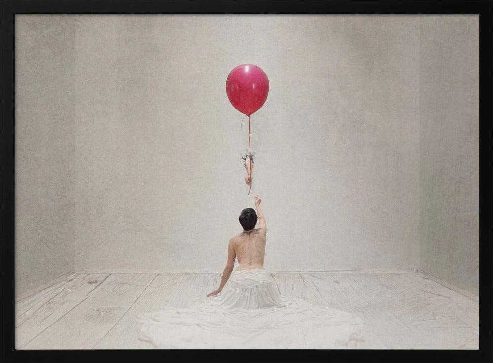 A surreal fine art photograph of a person with a bare back and a long white skirt, sitting on the floor of a minimalist grey room. They are reaching up towards a small figure hanging from the string of a large, bright red balloon that floats towards the ceiling. The image is enclosed in a silver frame. Artwork