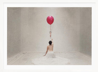 A surreal fine art photograph of a person with a bare back and a long white skirt, sitting on the floor of a minimalist grey room. They are reaching up towards a small figure hanging from the string of a large, bright red balloon that floats towards the ceiling. The image is enclosed in a silver frame. Artwork