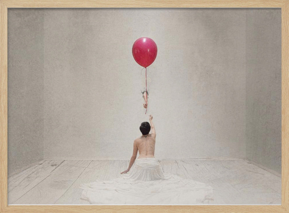 A surreal fine art photograph of a person with a bare back and a long white skirt, sitting on the floor of a minimalist grey room. They are reaching up towards a small figure hanging from the string of a large, bright red balloon that floats towards the ceiling. The image is enclosed in a silver frame. Artwork