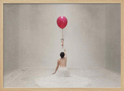 A surreal fine art photograph of a person with a bare back and a long white skirt, sitting on the floor of a minimalist grey room. They are reaching up towards a small figure hanging from the string of a large, bright red balloon that floats towards the ceiling. The image is enclosed in a silver frame. Artwork