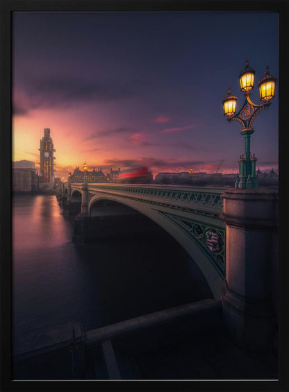 A breathtaking twilight view of Westminster Bridge in London, with the iconic Big Ben illuminated in the background against a purple and orange sunset sky. A vintage street lamp glows warmly in the foreground, and the motion blur of a red bus crosses the bridge over the calm River Thames. Print