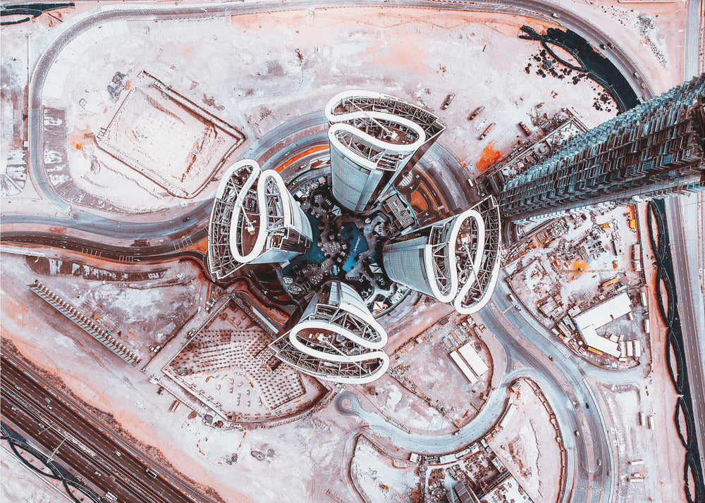 A dizzying top-down aerial photograph of five futuristic, petal-shaped skyscrapers surrounding a central turquoise pool. The surrounding urban landscape is a mix of dusty pink construction sites and curving roads, creating a surreal and abstract cityscape. Wall Art