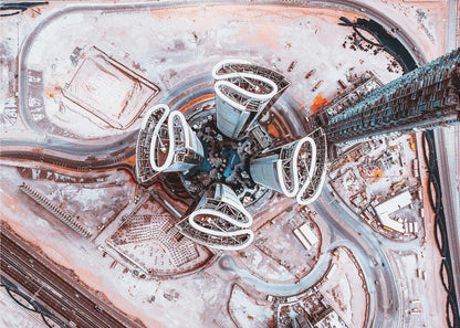 A dizzying top-down aerial photograph of five futuristic, petal-shaped skyscrapers surrounding a central turquoise pool. The surrounding urban landscape is a mix of dusty pink construction sites and curving roads, creating a surreal and abstract cityscape. Wall Art