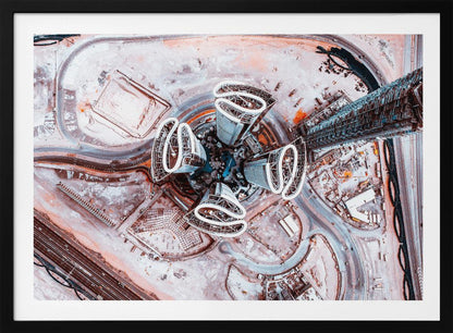 A dizzying top-down aerial photograph of five futuristic, petal-shaped skyscrapers surrounding a central turquoise pool. The surrounding urban landscape is a mix of dusty pink construction sites and curving roads, creating a surreal and abstract cityscape. Wall Art