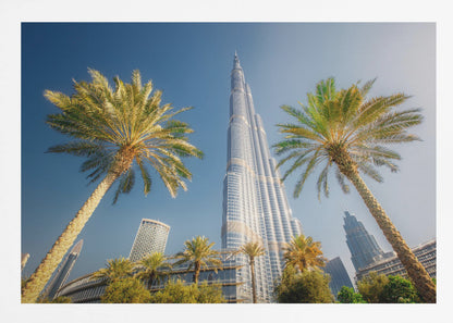 A low-angle photograph looking up at the towering Burj Khalifa skyscraper in Dubai, framed by two large palm trees against a clear, vibrant blue sky. Wall Art