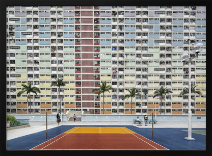 A wide, symmetrical photograph of the colorful Choi Hung Estate apartment building in Hong Kong, featuring a facade with a repeating pattern of pastel blue, green, yellow, and orange blocks. In front of the building is a vibrant basketball court painted in bold sections of blue, red, and yellow, with several palm trees lining the courtyard. Print