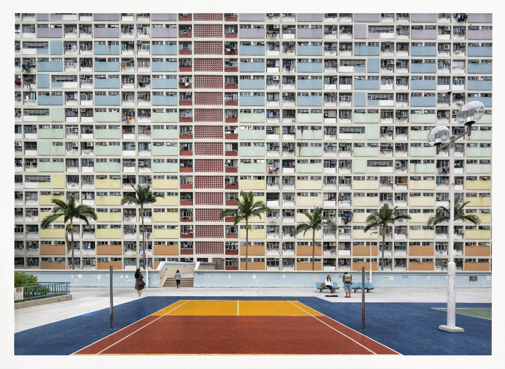 A wide, symmetrical photograph of the colorful Choi Hung Estate apartment building in Hong Kong, featuring a facade with a repeating pattern of pastel blue, green, yellow, and orange blocks. In front of the building is a vibrant basketball court painted in bold sections of blue, red, and yellow, with several palm trees lining the courtyard. Print