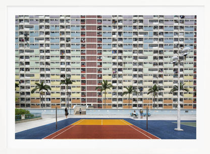 A wide, symmetrical photograph of the colorful Choi Hung Estate apartment building in Hong Kong, featuring a facade with a repeating pattern of pastel blue, green, yellow, and orange blocks. In front of the building is a vibrant basketball court painted in bold sections of blue, red, and yellow, with several palm trees lining the courtyard. Print