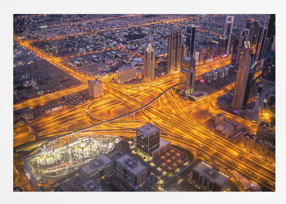 A stunning aerial view of a futuristic city at night, with brilliantly lit highways forming intricate patterns of golden light amidst towering skyscrapers, enclosed in a silver frame. Poster