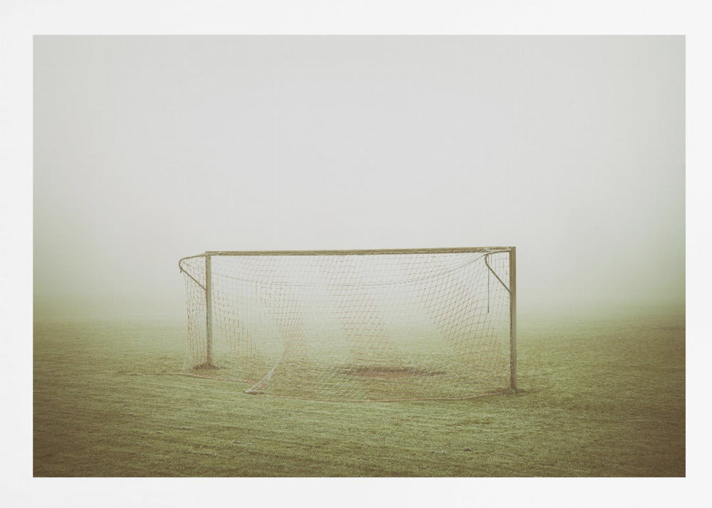 A framed photograph of an empty soccer goal with a net, standing alone on a green grass field enveloped in thick, white fog, creating a minimalist and atmospheric scene. Poster