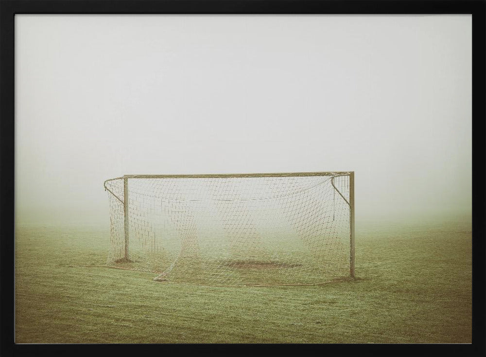 A framed photograph of an empty soccer goal with a net, standing alone on a green grass field enveloped in thick, white fog, creating a minimalist and atmospheric scene. Poster