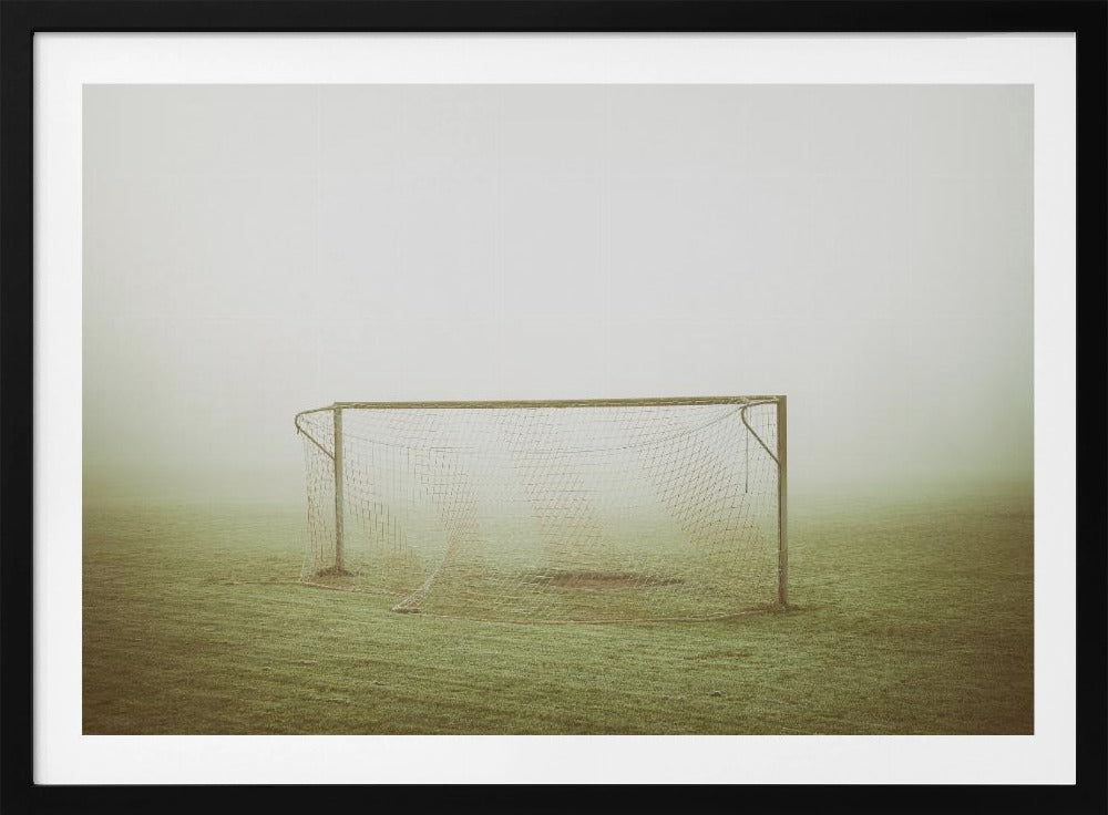 A framed photograph of an empty soccer goal with a net, standing alone on a green grass field enveloped in thick, white fog, creating a minimalist and atmospheric scene. Poster