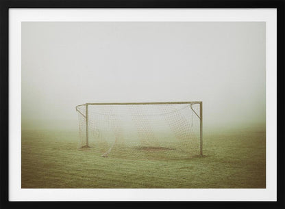 A framed photograph of an empty soccer goal with a net, standing alone on a green grass field enveloped in thick, white fog, creating a minimalist and atmospheric scene. Poster