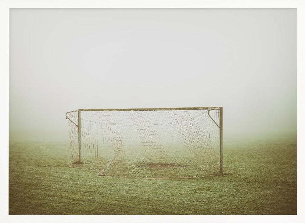 A framed photograph of an empty soccer goal with a net, standing alone on a green grass field enveloped in thick, white fog, creating a minimalist and atmospheric scene. Poster