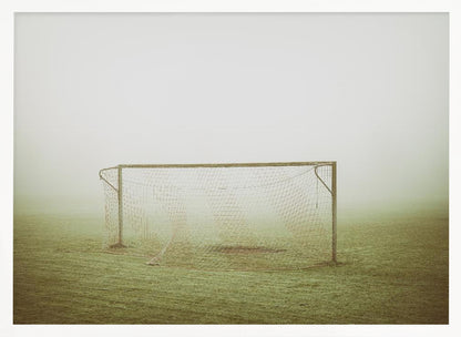 A framed photograph of an empty soccer goal with a net, standing alone on a green grass field enveloped in thick, white fog, creating a minimalist and atmospheric scene. Poster