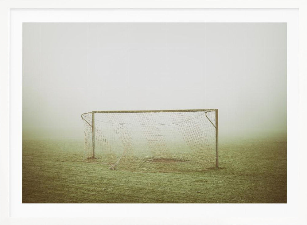 A framed photograph of an empty soccer goal with a net, standing alone on a green grass field enveloped in thick, white fog, creating a minimalist and atmospheric scene. Poster