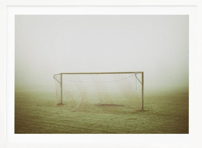 A framed photograph of an empty soccer goal with a net, standing alone on a green grass field enveloped in thick, white fog, creating a minimalist and atmospheric scene. Poster