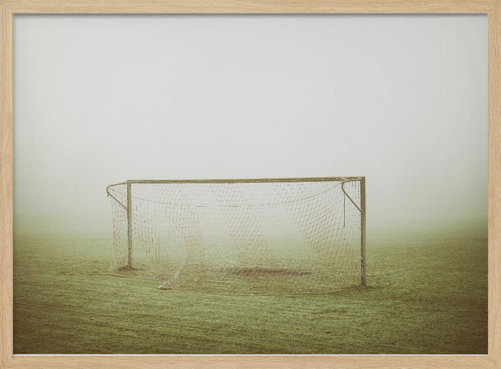 A framed photograph of an empty soccer goal with a net, standing alone on a green grass field enveloped in thick, white fog, creating a minimalist and atmospheric scene. Poster