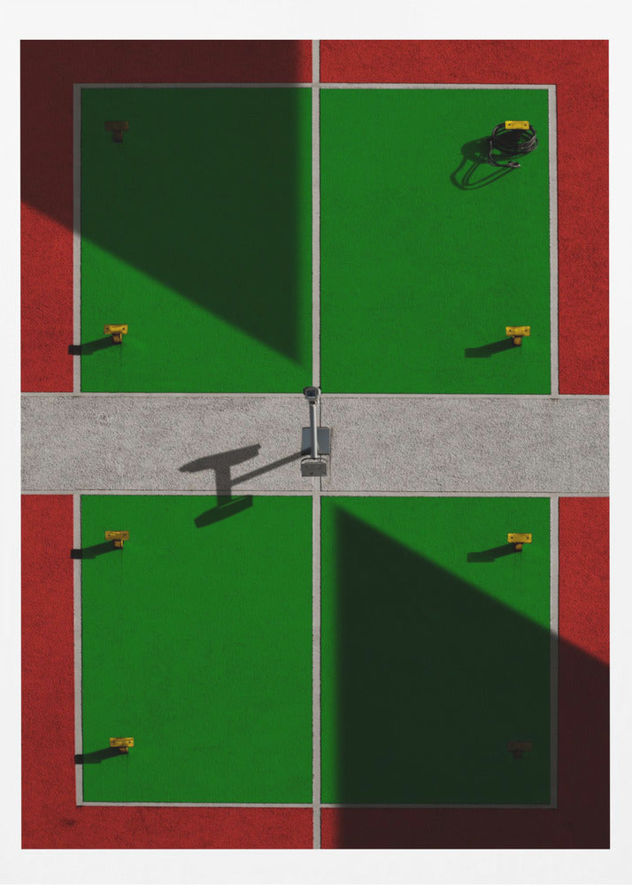 A high-angle, symmetrical photograph of a green and red sports court, viewed from directly above. Strong, sharp shadows cut diagonally across the composition, creating a geometric and abstract pattern of light and dark. A net post in the center casts a T-shaped shadow on the concrete dividing strip. Print