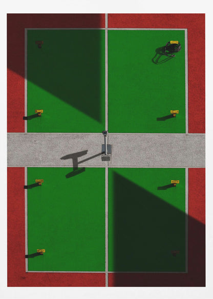 A high-angle, symmetrical photograph of a green and red sports court, viewed from directly above. Strong, sharp shadows cut diagonally across the composition, creating a geometric and abstract pattern of light and dark. A net post in the center casts a T-shaped shadow on the concrete dividing strip. Print