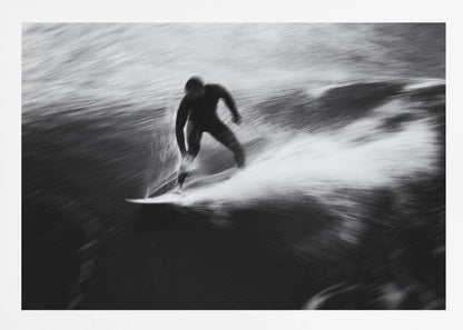 A dynamic black and white photograph of a surfer in a wetsuit carving through a wave. The image uses motion blur to emphasize the speed and energy of the water, creating a powerful and artistic effect. The artwork is presented in a simple silver frame. Print