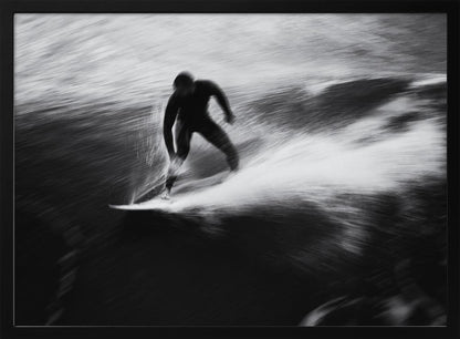 A dynamic black and white photograph of a surfer in a wetsuit carving through a wave. The image uses motion blur to emphasize the speed and energy of the water, creating a powerful and artistic effect. The artwork is presented in a simple silver frame. Print