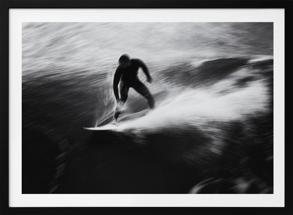 A dynamic black and white photograph of a surfer in a wetsuit carving through a wave. The image uses motion blur to emphasize the speed and energy of the water, creating a powerful and artistic effect. The artwork is presented in a simple silver frame. Print