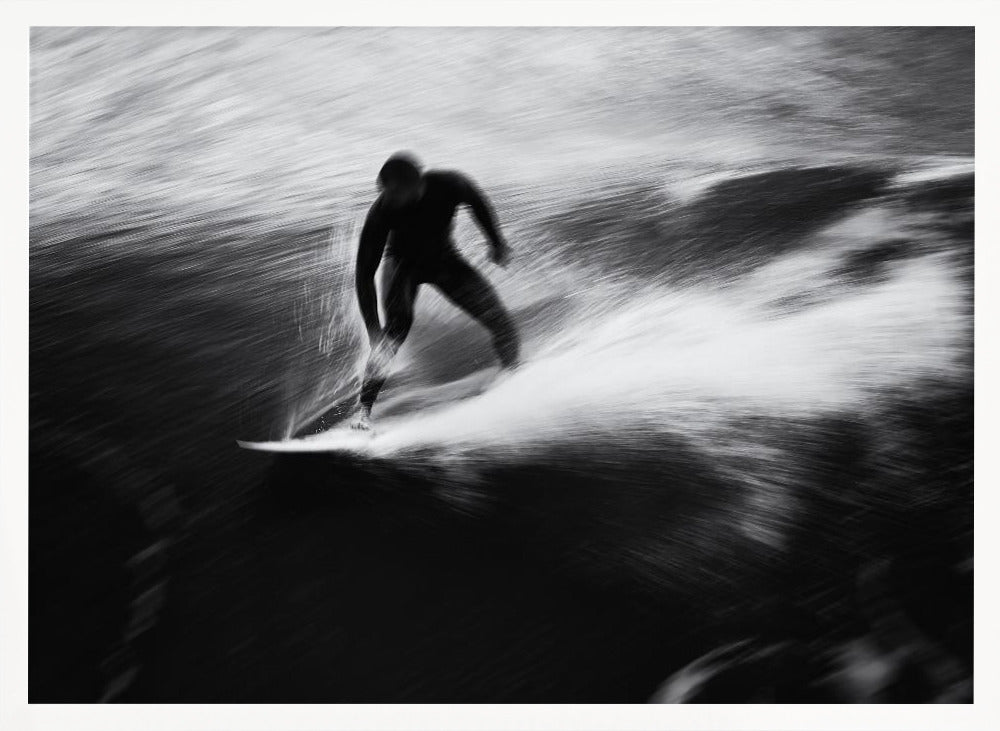 A dynamic black and white photograph of a surfer in a wetsuit carving through a wave. The image uses motion blur to emphasize the speed and energy of the water, creating a powerful and artistic effect. The artwork is presented in a simple silver frame. Print