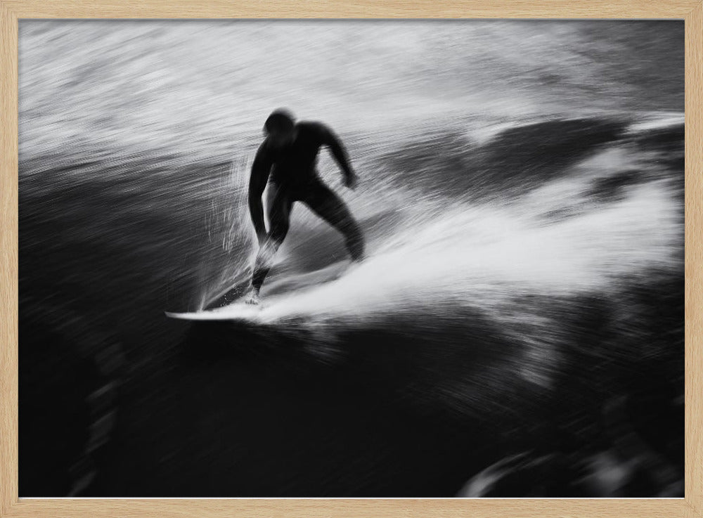 A dynamic black and white photograph of a surfer in a wetsuit carving through a wave. The image uses motion blur to emphasize the speed and energy of the water, creating a powerful and artistic effect. The artwork is presented in a simple silver frame. Print
