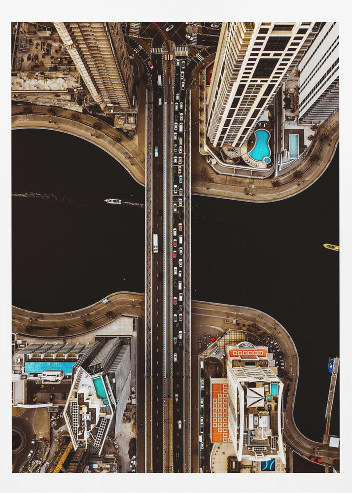 A symmetrical, top-down aerial photograph of a busy city bridge crossing dark water, flanked by towering skyscrapers with bright blue rooftop swimming pools. Print