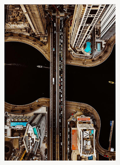 A symmetrical, top-down aerial photograph of a busy city bridge crossing dark water, flanked by towering skyscrapers with bright blue rooftop swimming pools. Print