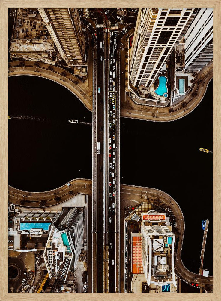 A symmetrical, top-down aerial photograph of a busy city bridge crossing dark water, flanked by towering skyscrapers with bright blue rooftop swimming pools. Print