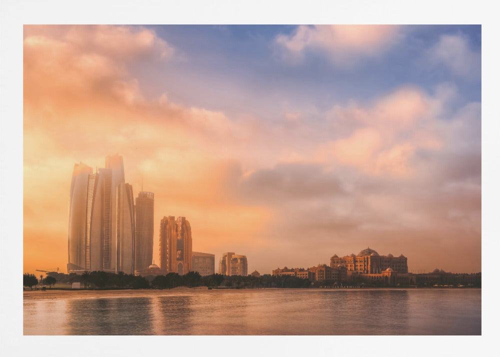 A framed photograph of the Abu Dhabi city skyline at sunset, featuring modern skyscrapers and the Emirates Palace hotel glowing in warm, orange light. The buildings are reflected in the calm water of the foreground, under a sky with soft orange and blue clouds. Poster