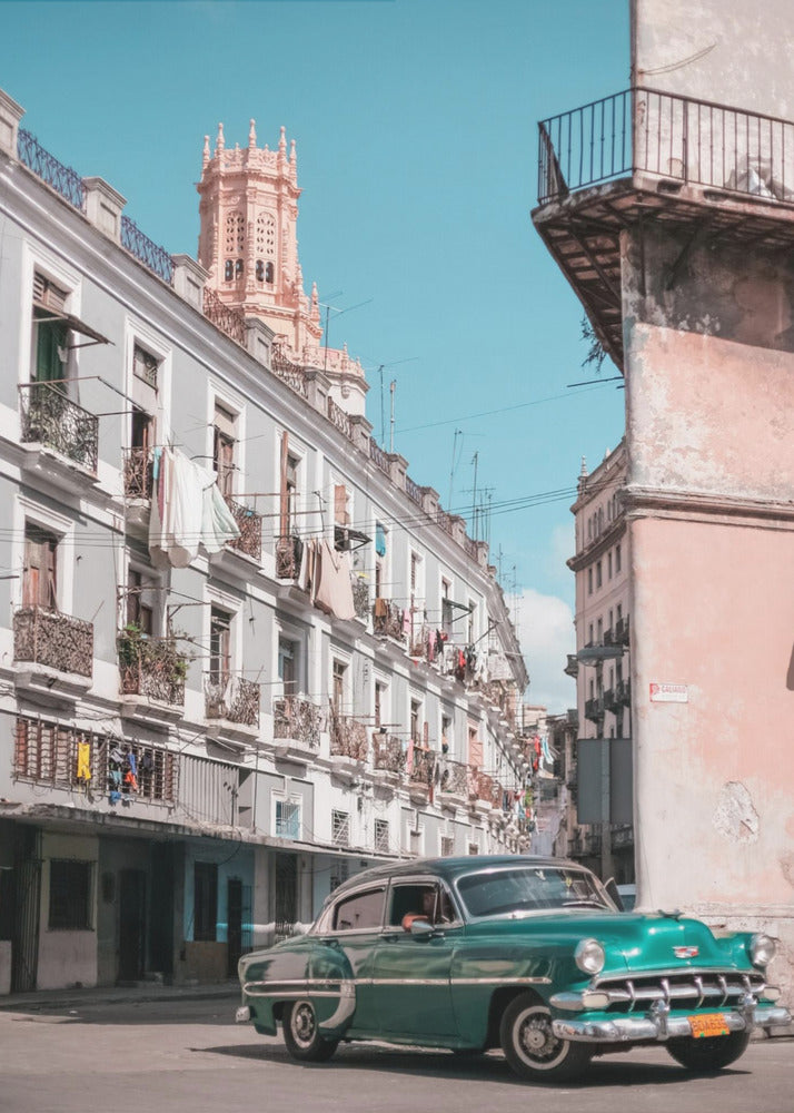 A vintage teal-green classic car sits on a sunny street in a historic city, possibly Havana, Cuba. Weathered apartment buildings with intricate balconies and hanging laundry line the street, with a peach-colored church tower visible in the background against a clear turquoise sky. Poster